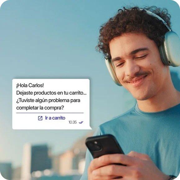 Hombre sonriendo mientras mira su celular, ilustrando la recepción de un mensaje de WhatsApp automatizado para recuperar un carrito abandonado en un eCommerce